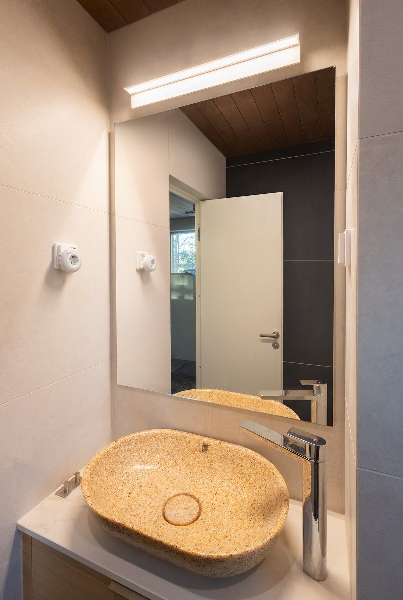 In a small toilet, a minimalist white wall lamp 60 centimetres in length elegantly illuminates the mirror. The light has a colour temperature of 3 000 Kelvin.